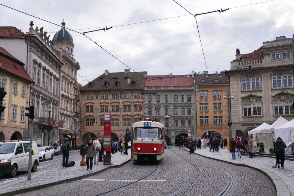 Red tram passing through a historic square in Prague