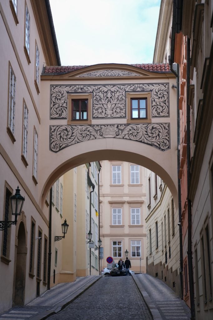 Cobblestone lane beneath a decorative arch in Malá Strana