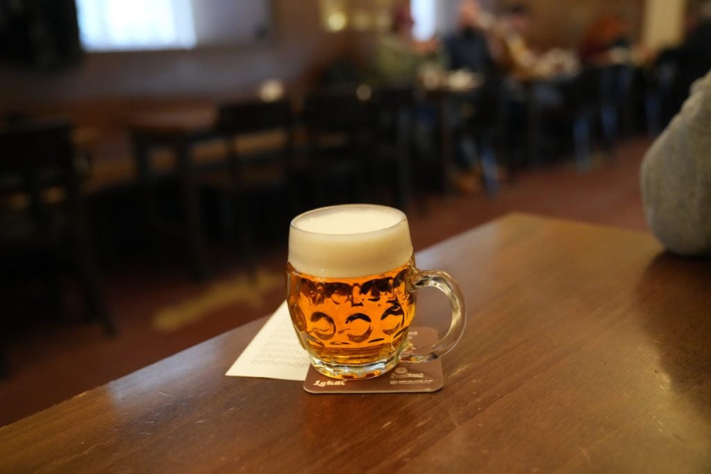 Small glass mug of pale beer on a wooden pub table
