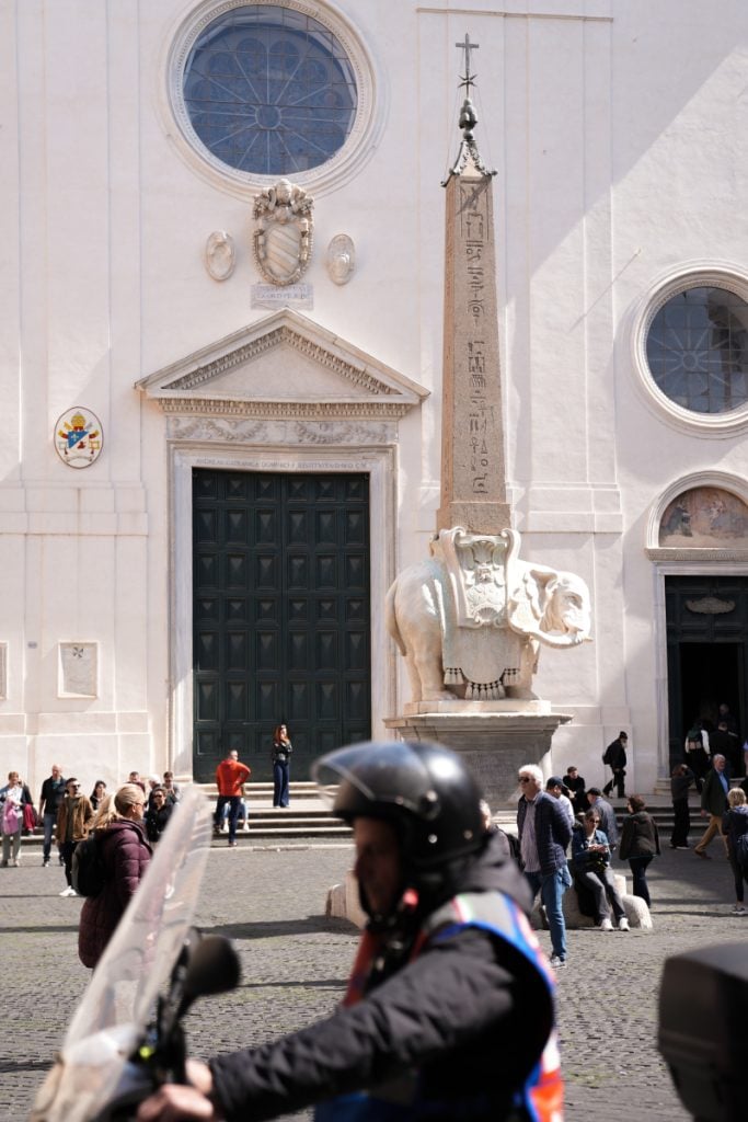 Scooter rider passing the Elephant and Obelisk monument in Rome