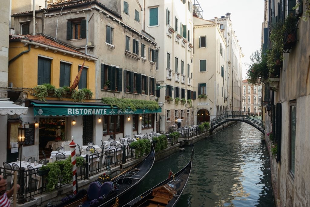 Gondolas beside a canal restaurant and footbridge in Venice