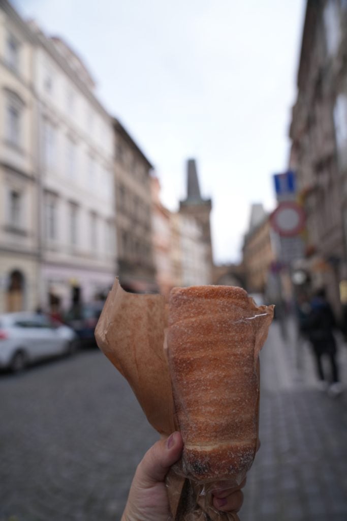 Hand holding a cinnamon-sugar trdelník on a Prague street