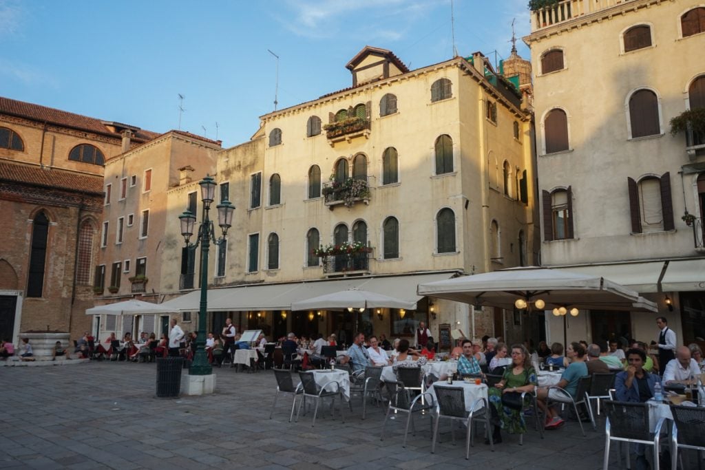 Diners at outdoor restaurant tables in a Venice square