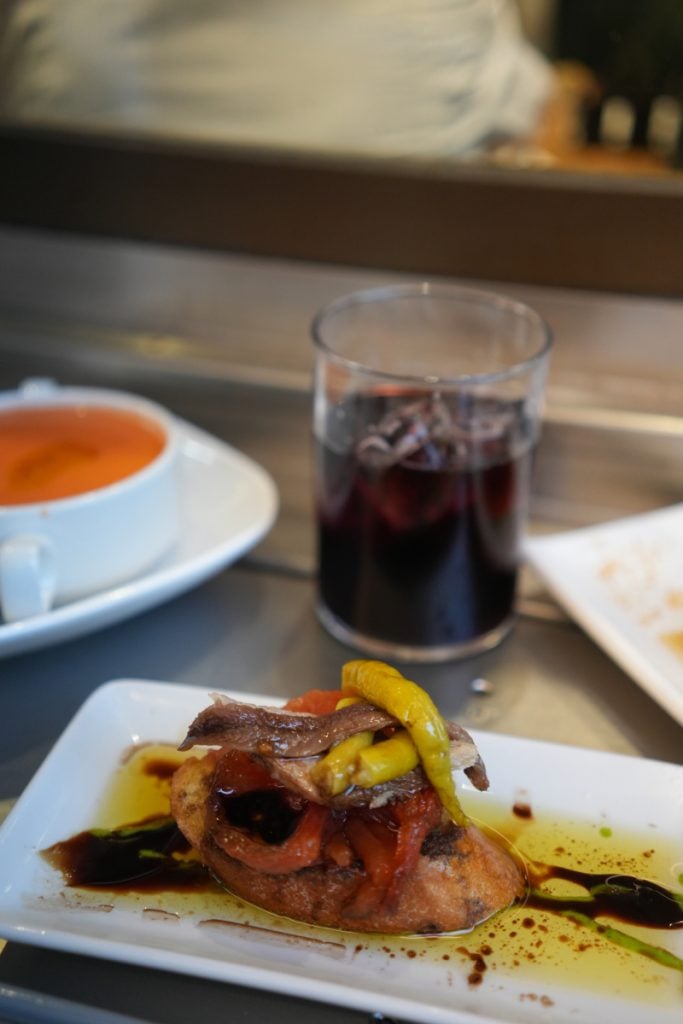 Anchovy and pepper pintxo beside a glass of red wine