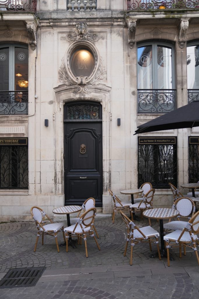 Outdoor café tables beside an ornate stone facade in Bayonne