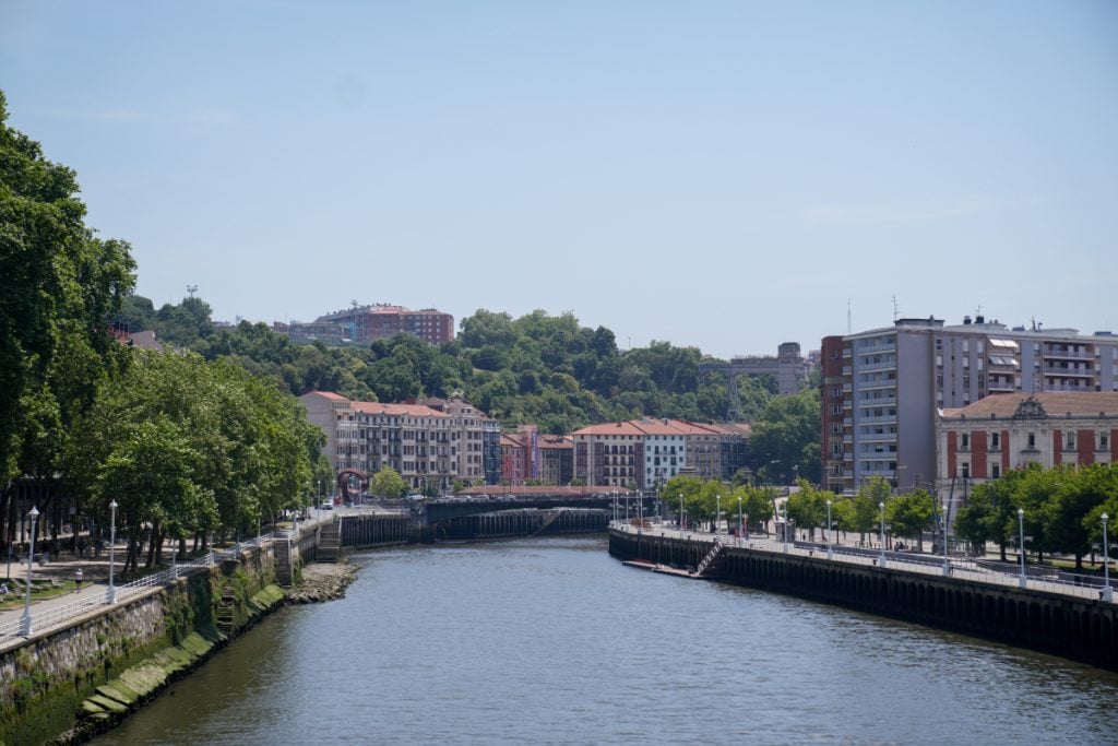 Tree-lined riverbanks and hillside buildings in Castaños, Bilbao