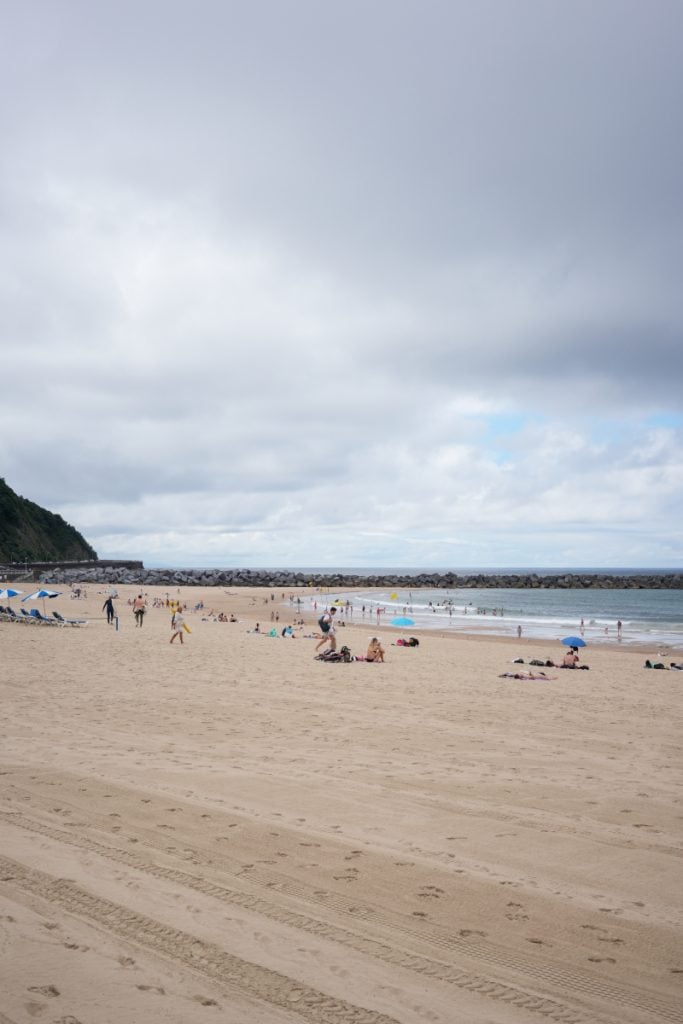 Beachgoers on Zurriola Beach under cloudy skies