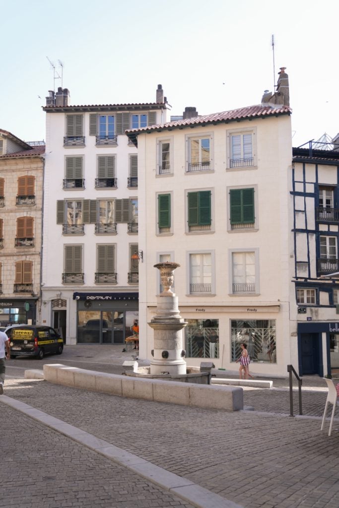 Stone fountain in a Bayonne square lined with shuttered buildings