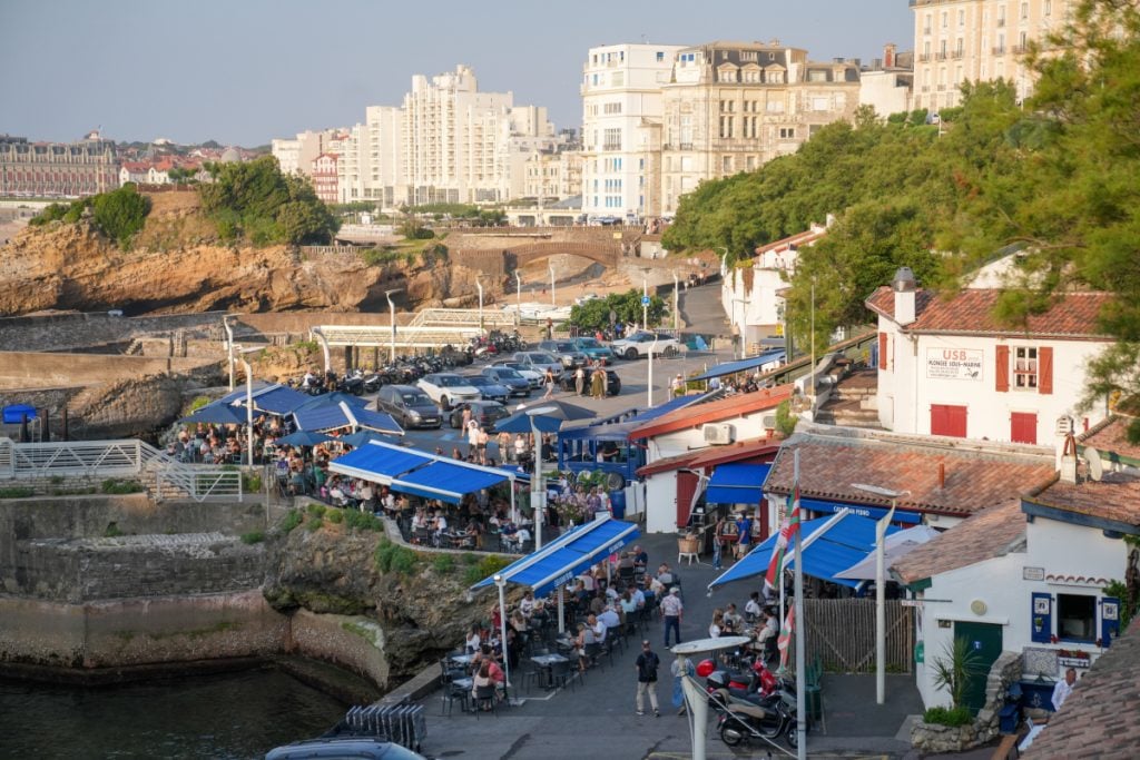 Busy waterfront restaurants beneath hillside buildings in Biarritz