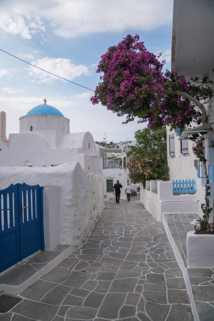 Stone-paved lane with a blue-domed church and pink bougainvillea in Apollonia.