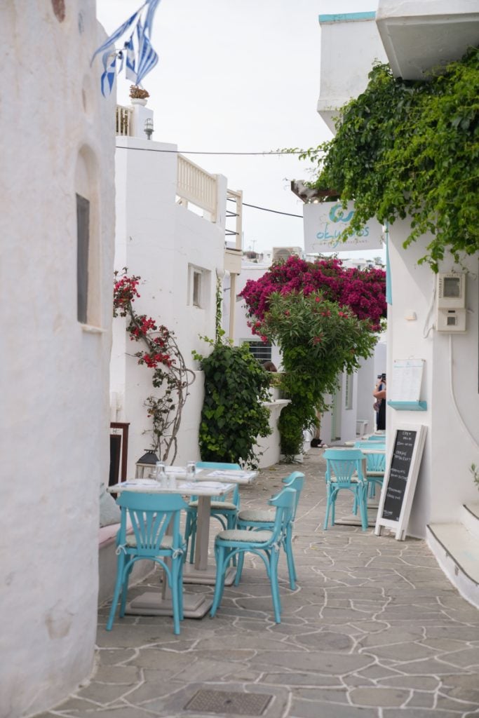 Turquoise cafe chairs and tables along a flower-lined lane in Apollonia.