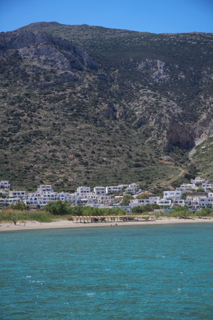 Kamares beach and white waterfront buildings beneath a steep rocky mountain.