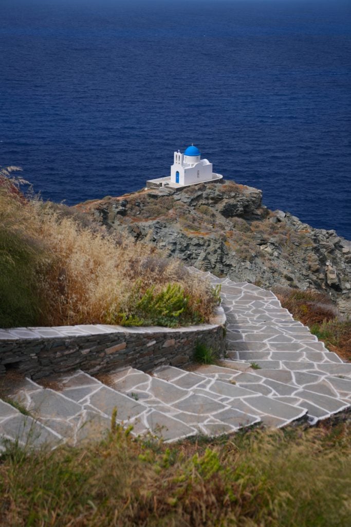 Stone steps descending to a blue-domed church on a rocky headland below Kastro.