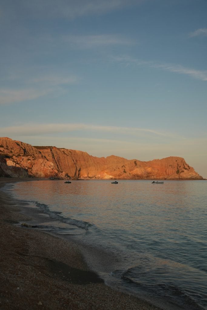 Sunlit cliffs and anchored boats at Paleochori Beach