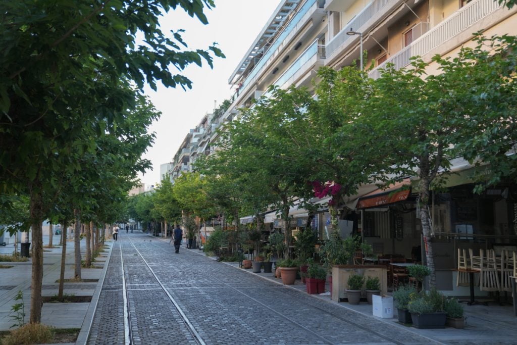 Tree-lined Plaka street with cafés and rail tracks