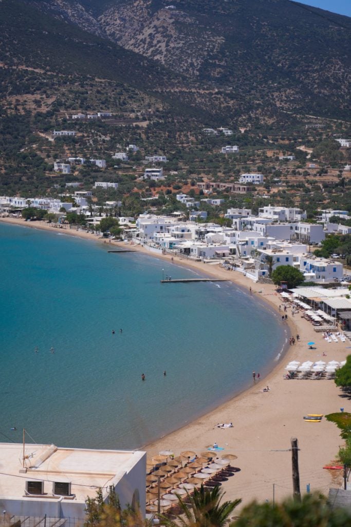 Platis Gialos beach curving around a turquoise bay below white hillside buildings.