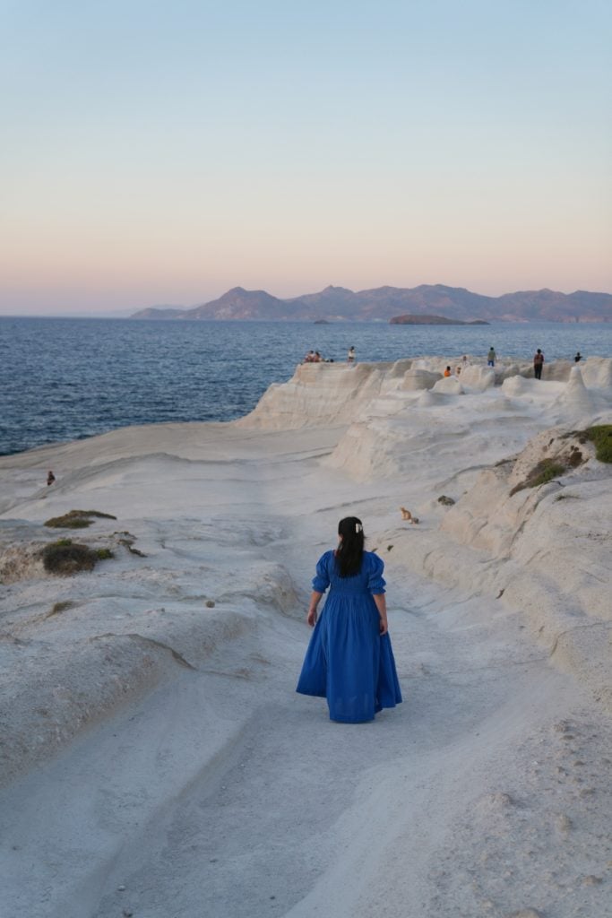 Woman in blue dress walking across Sarakiniko's white cliffs