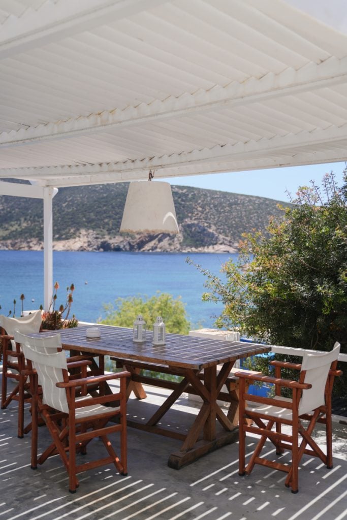 Shaded dining terrace with wooden chairs overlooking Vathi Bay.