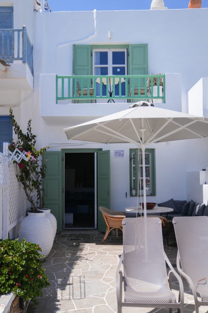 Villa Glaros facade with mint-green shutters, a balcony and a shaded patio.