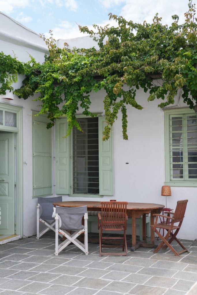 Vine-shaded courtyard with green shutters in Artemonas