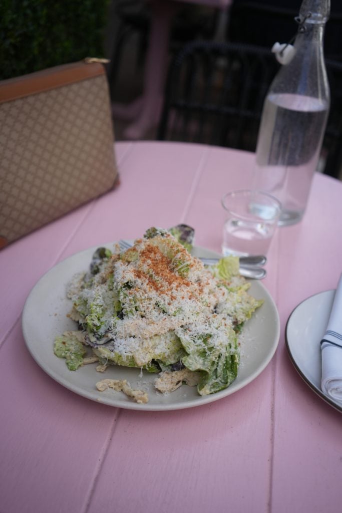 Green salad topped with grated cheese on a pink table at Bettina