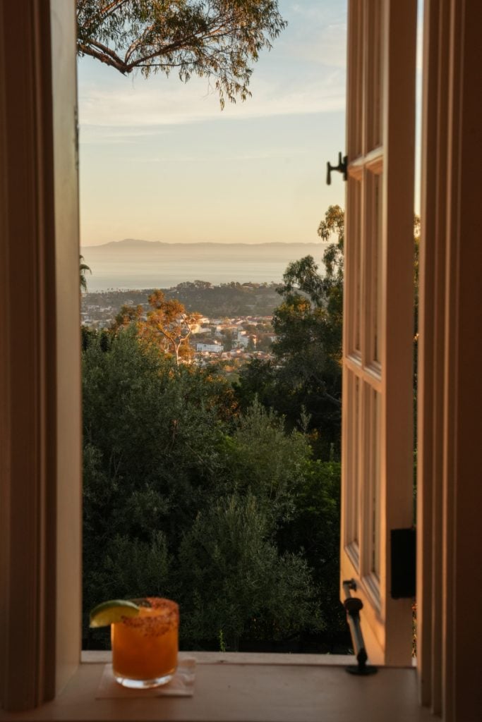 Ocean view through an open window at El Encanto, with a drink on the windowsill