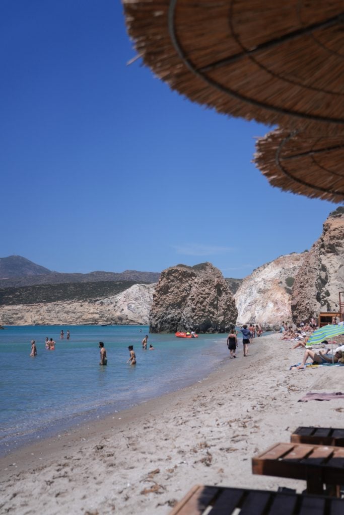 Swimmers along Firiplaka Beach beneath rocky cliffs