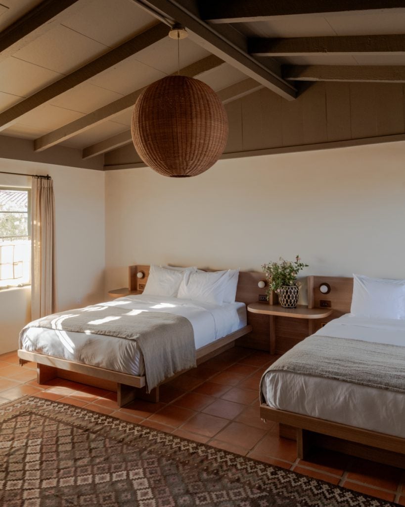 Hotel Wren guest room with two beds, exposed beams and a woven pendant light