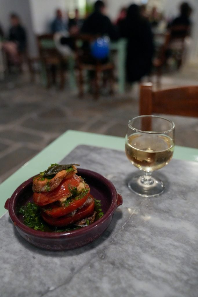Layered tomato dish with herbs beside a glass of wine