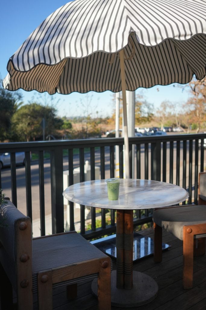 Green iced drink on a patio table beneath a striped umbrella at Little King Coffee