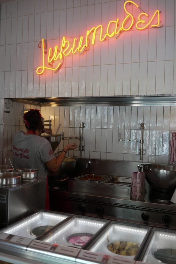 Employee preparing loukoumades beneath the LUKUMAΔΕΣ sign