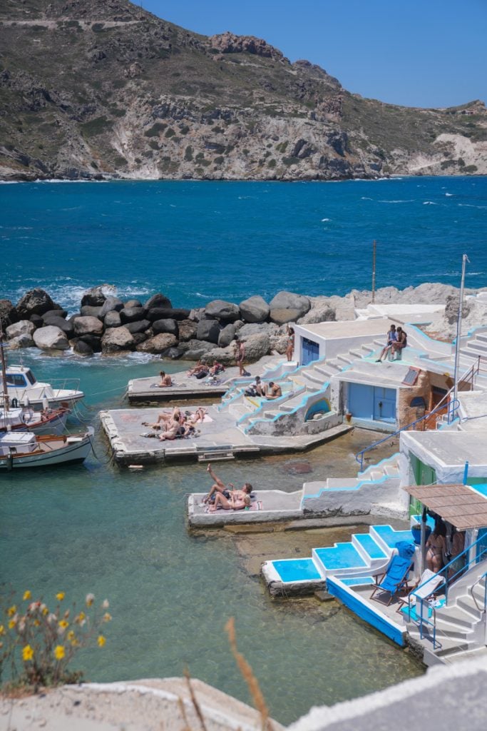 People sunbathe beside waterfront boathouses in Mandrakia