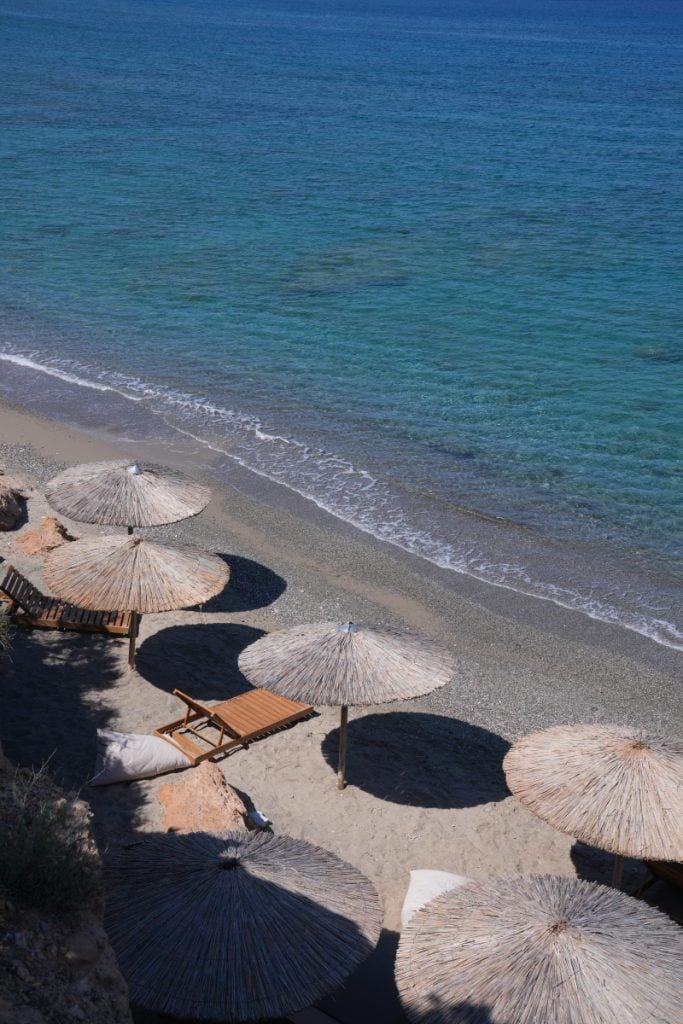 Straw umbrellas and loungers along a pebbly Paros beach