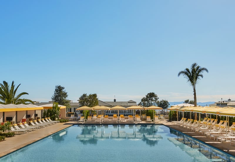 Swimming pool lined with yellow umbrellas and lounge chairs at Rosewood Miramar Beach