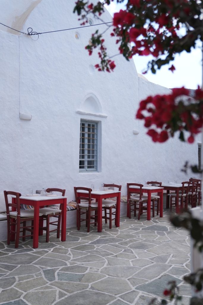 Red taverna tables beside a whitewashed wall in Apollonia