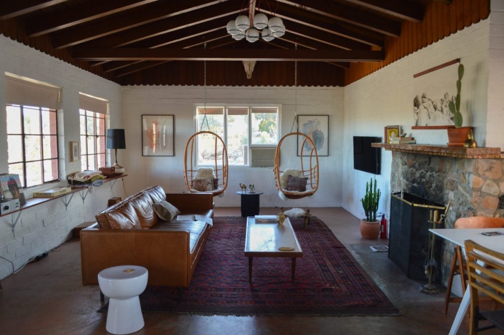The Joshua Tree House living room with hanging chairs, a leather sofa and stone fireplace