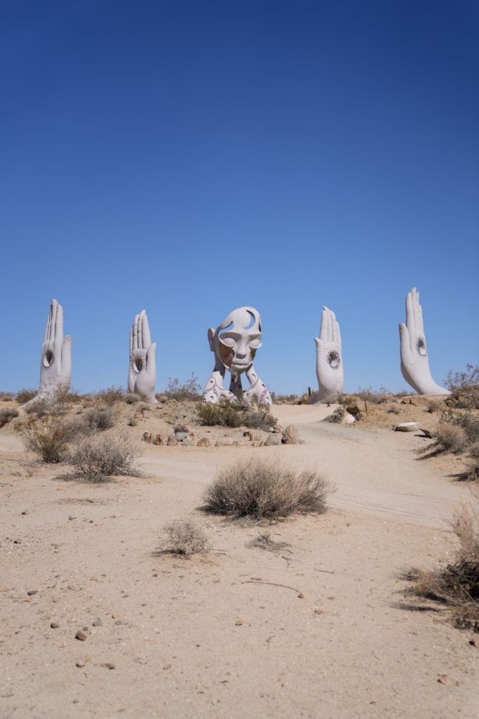 Transmission sculpture with a central head and raised hands in the Joshua Tree desert