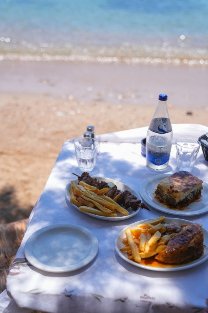 Plates of grilled meat and fries beside Vathi Beach